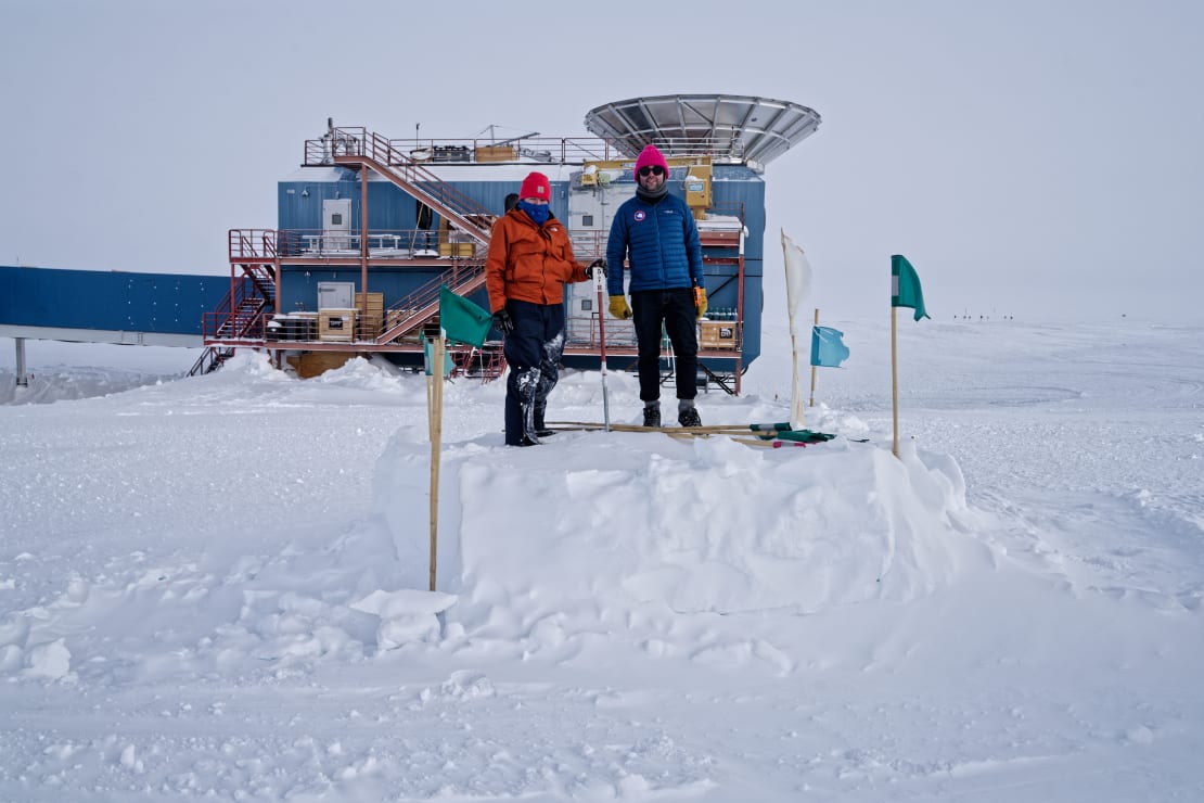 Two winterovers standing in front of South Pole Telescope.