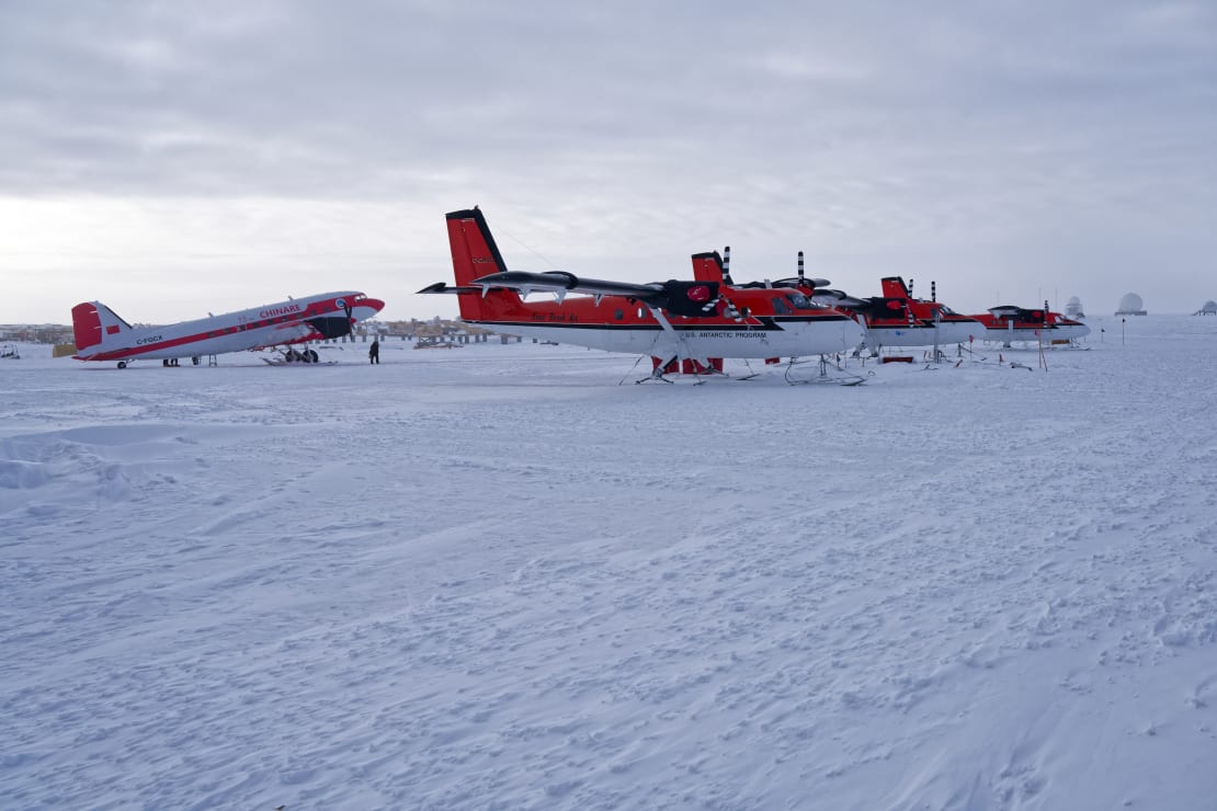 Small plane on the ice parked behind three other small aircraft.