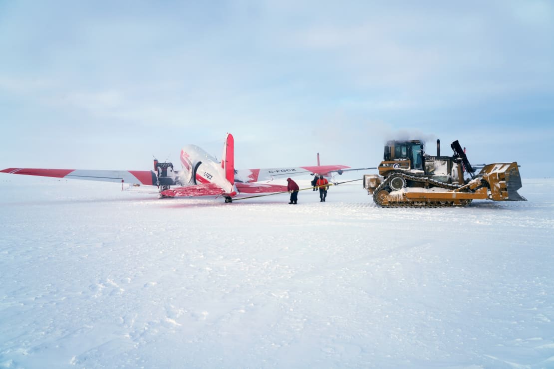 Small plane on the ice being pulled by a bulldozer.