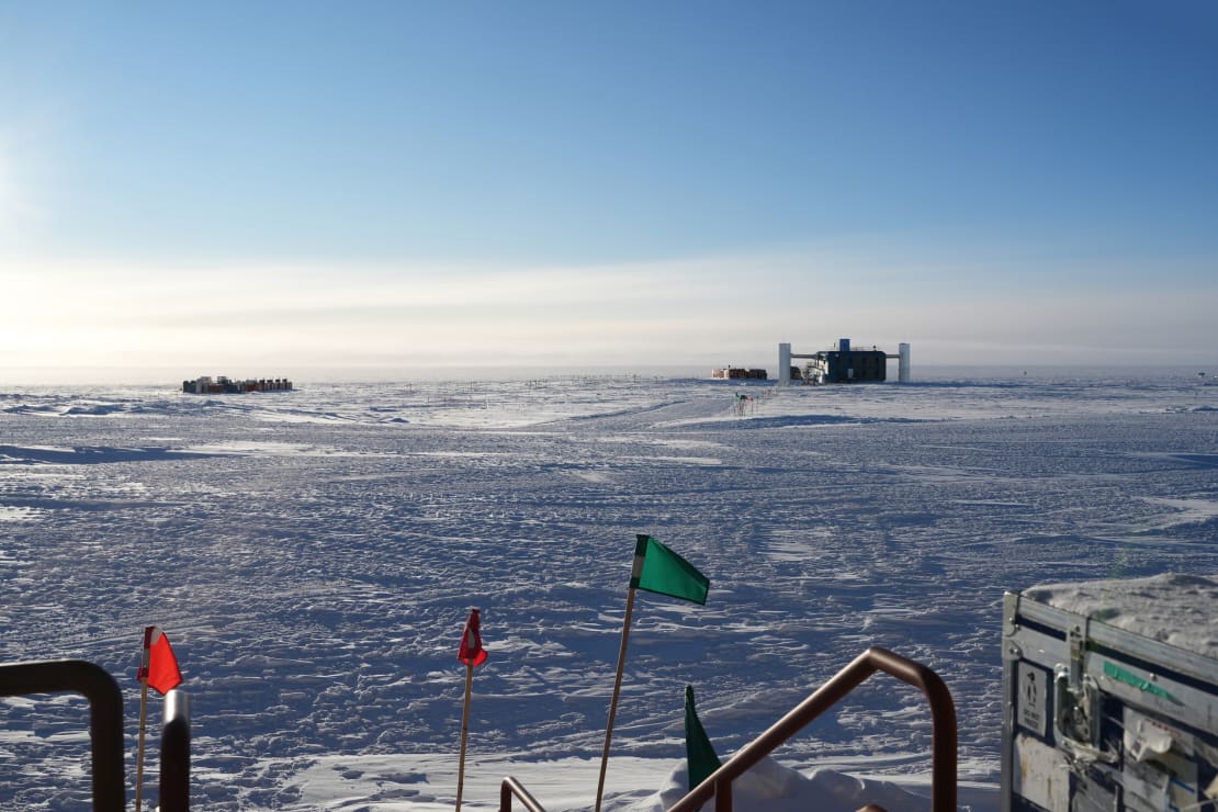 Blue skies with some wispy low clouds above the IceCube Lab in the distance.