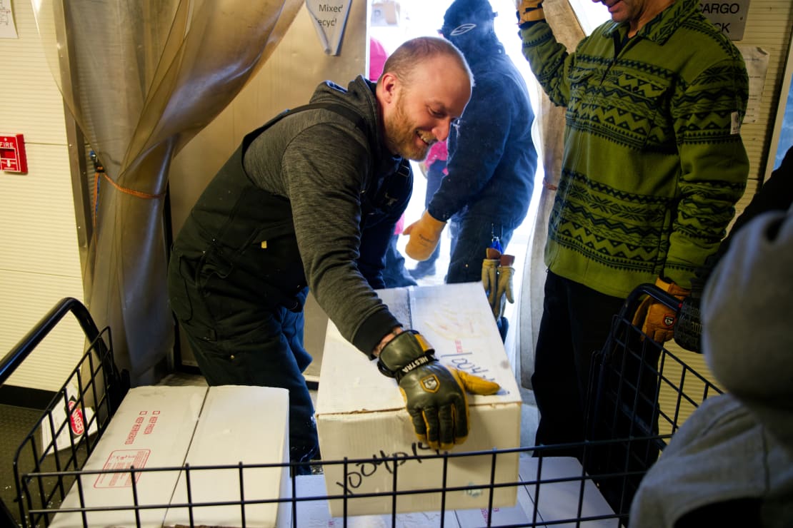 A person lifting a box off a cart of boxes, with others waiting in assembly line fashion.