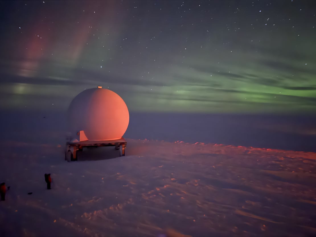 Some not too bright green auroras filling the sky, with a satellite dome partially lit in view.