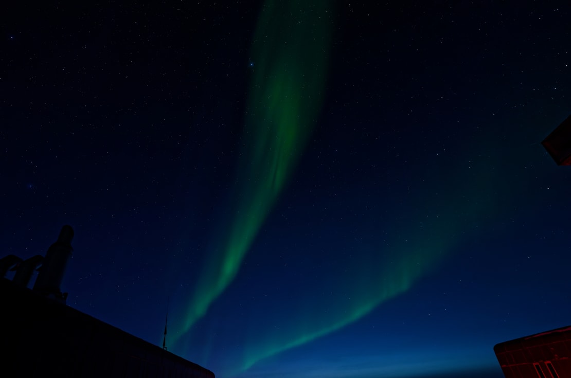 Two curvy green streaks of auroras against a dark, slightly blue sky.