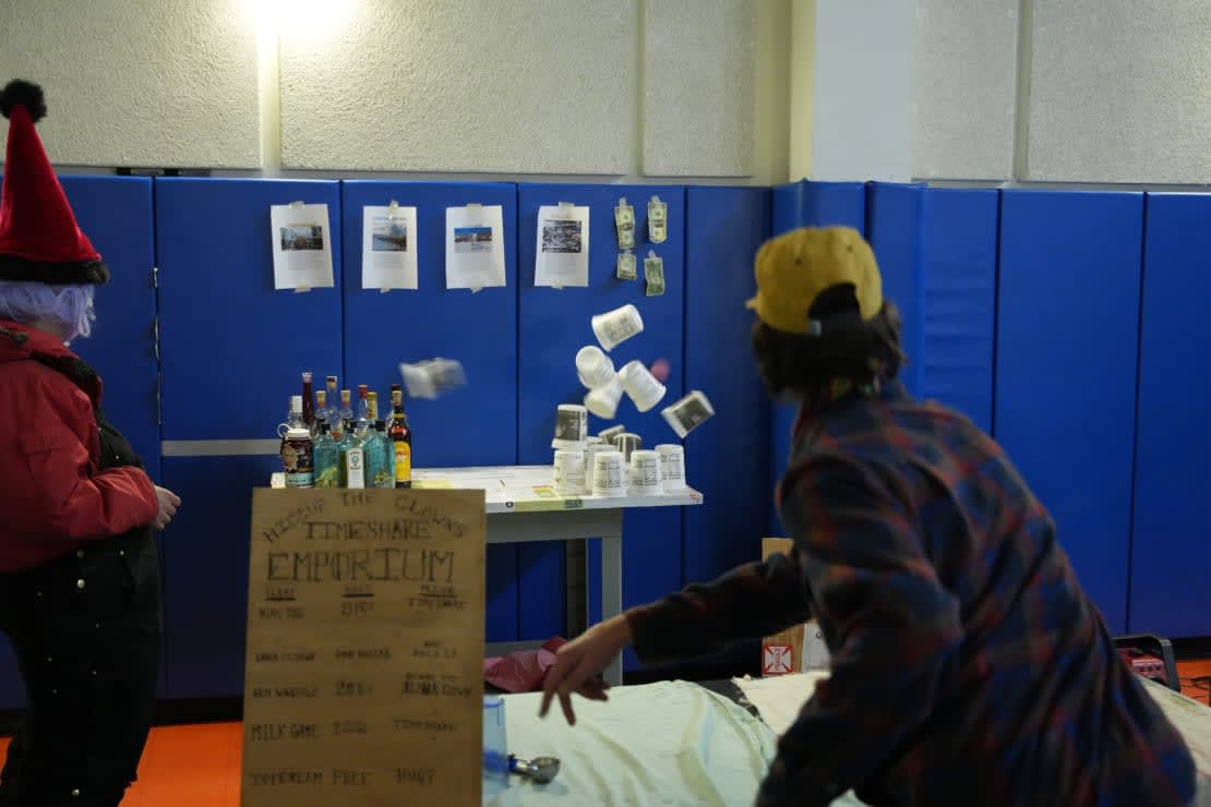 Person seen from behind, throwing ball to knock down tower of containers on a table.