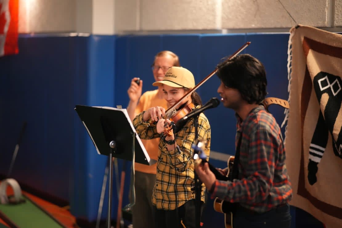Two people playing stringed instruments in front of a music stand.