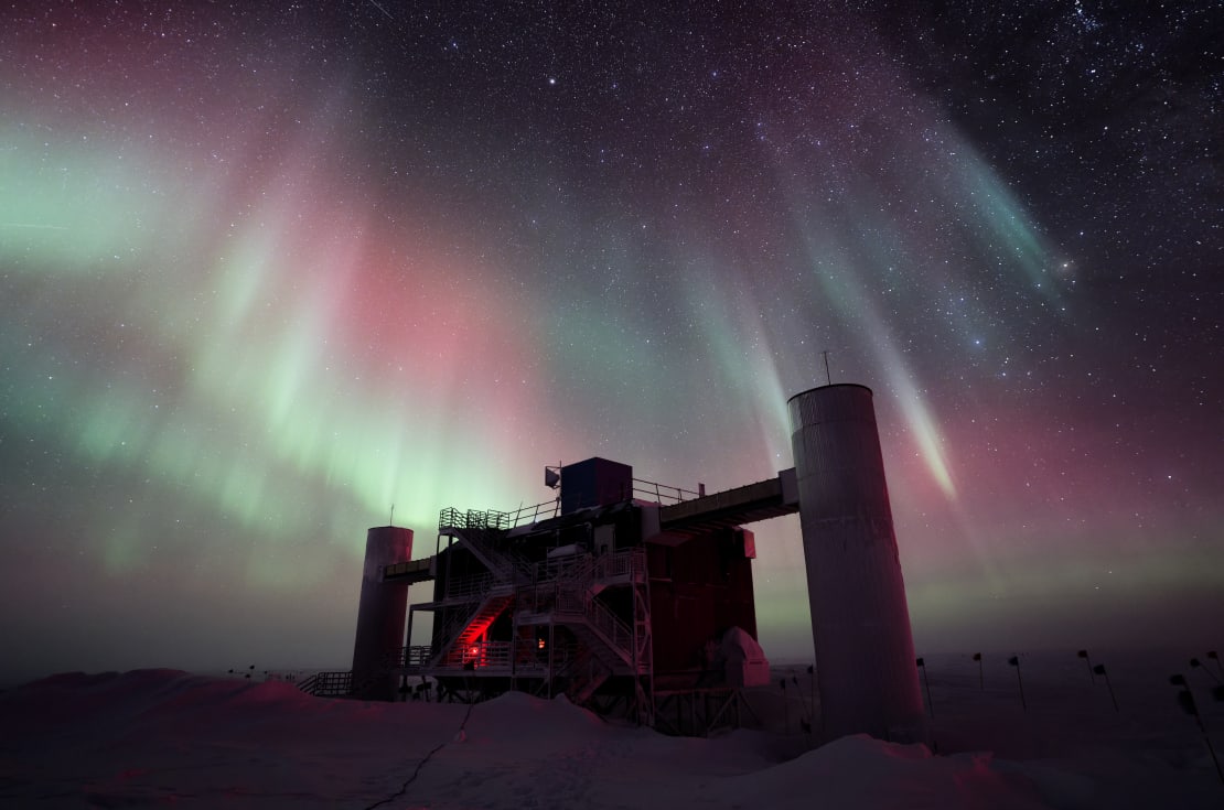 Multicolored auroras fanning out across sky above IceCube Lab, in full shadow.