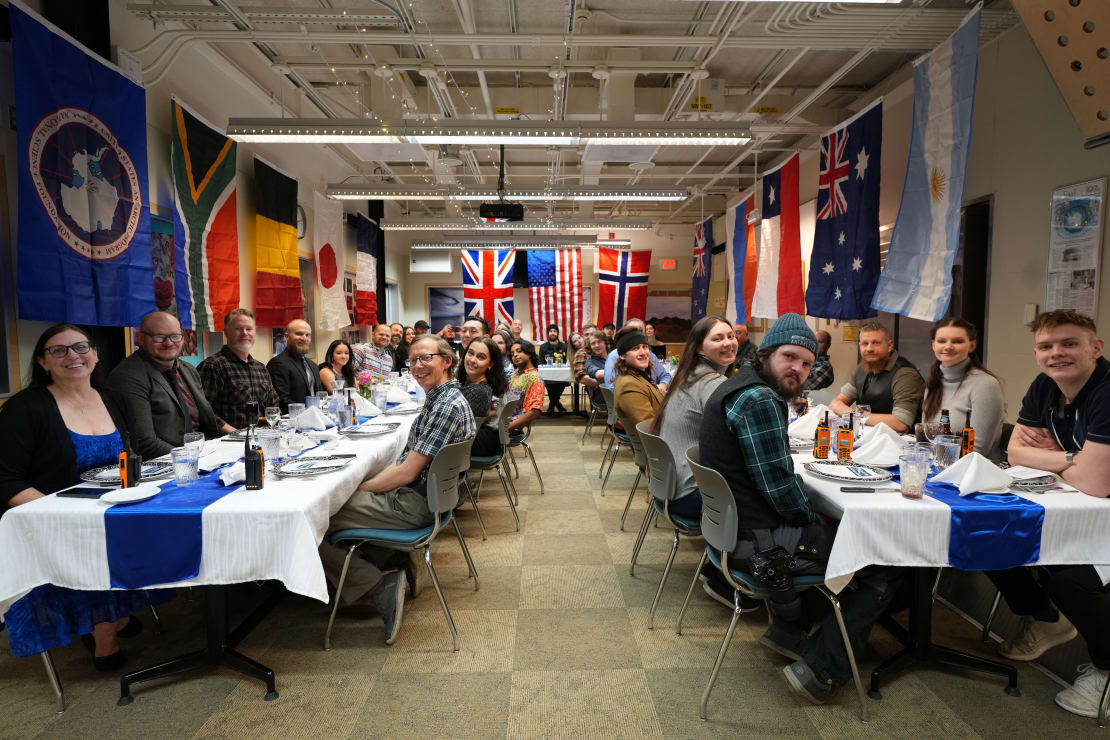 Station staff all facing the camera while seated at two long dining tables.