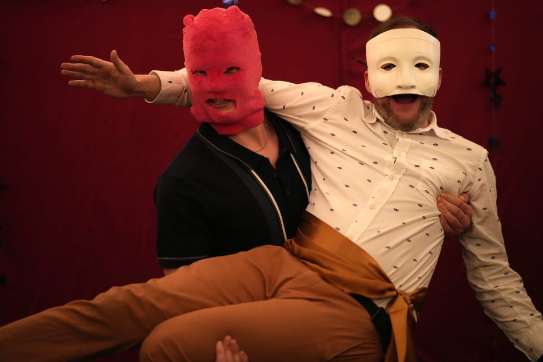 Close-up of two masked partygoers, one held in the arms of the other.