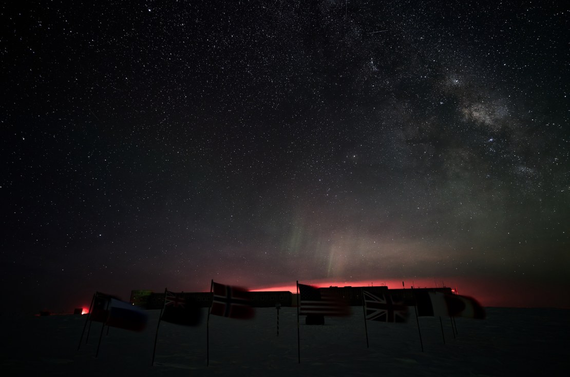 Star-filled dark winter sky a the Pole, with the top of the station outlined from red backlight.