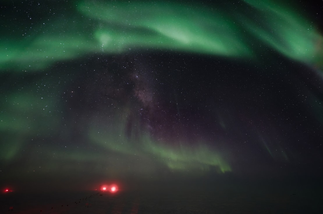 Green auroras swirling across sky with stars in dark sky peaking through gaps.