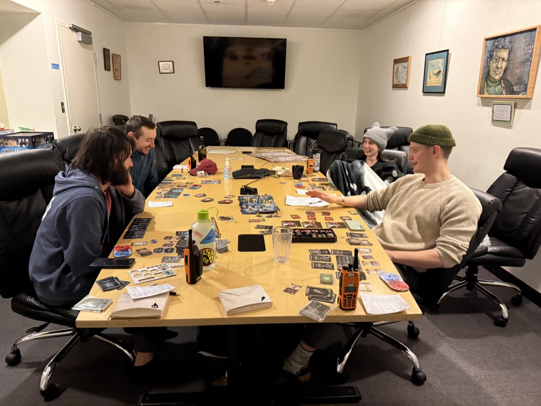 Four winterovers engaged in board game on a long conference room table.