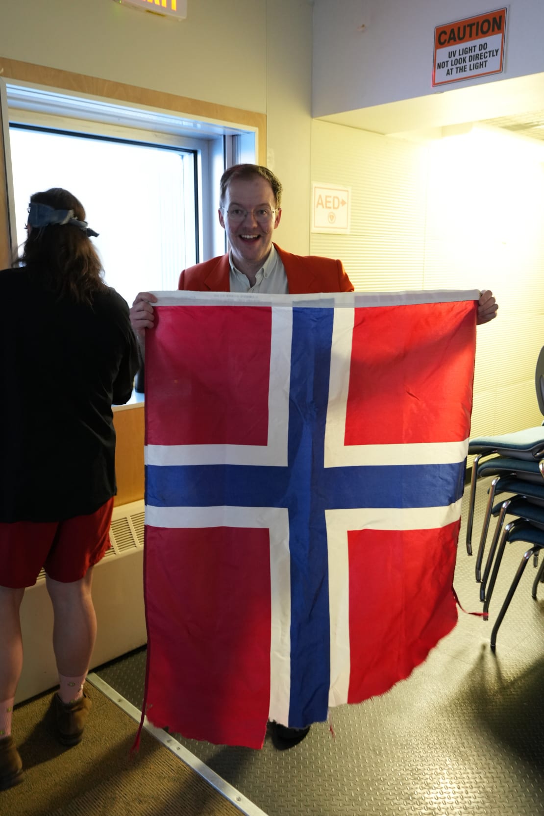 Smiling person holding up a battered Norwegian flag.
