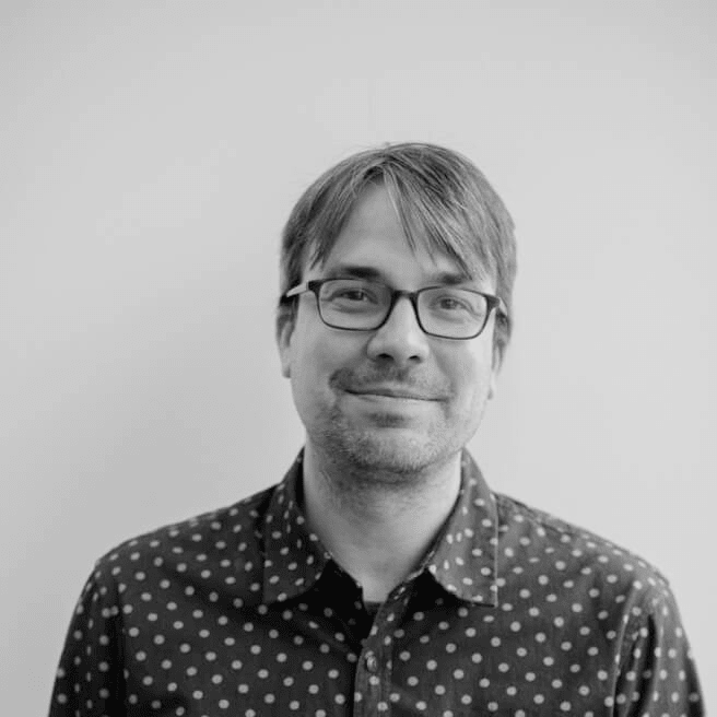 A headshot of a man with glasses in black and white