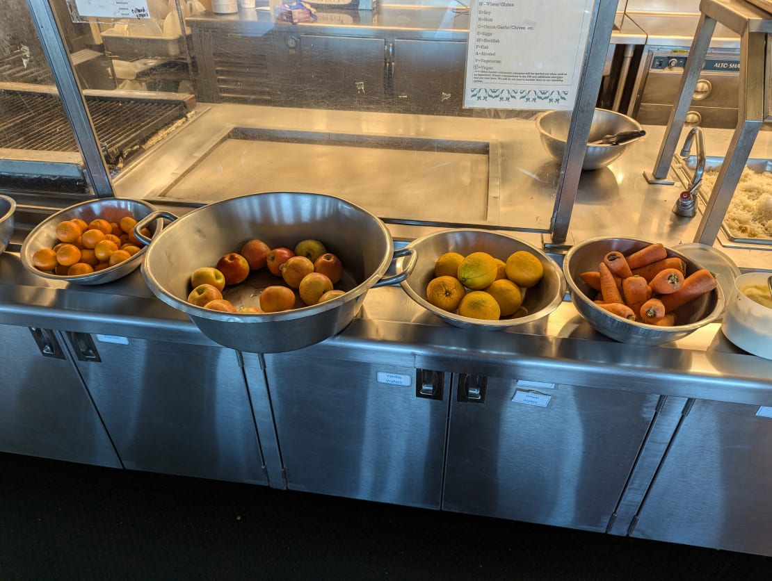 Several large bowls of fresh fruits and vegetables lined up on counter.