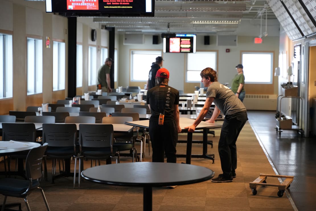 Long view of South Pole station galley with several people in the midst of organizing groups of tables and chairs.