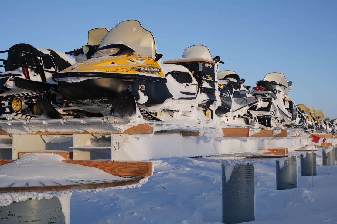 A line of snow-covered snowmobiles stacked on spools in the South Pole storage berms.