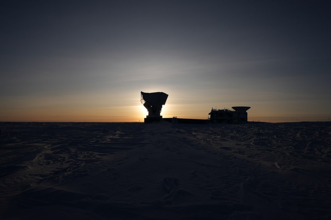 Sunrise at South Pole, with low sun directly behind South Pole Telescope, leaving surroundings in dark and shadow.
