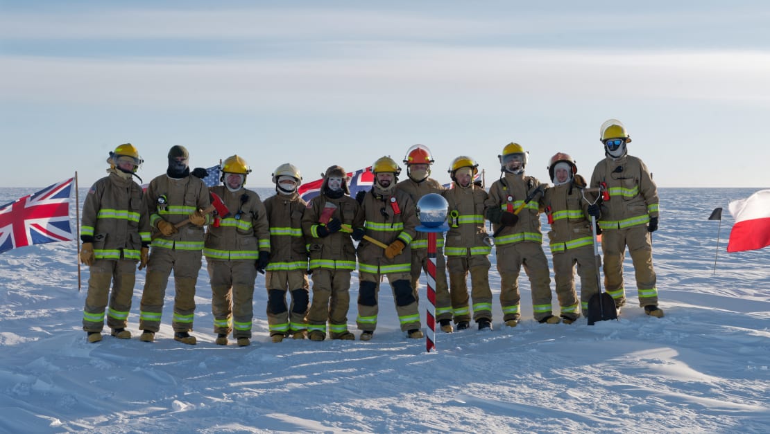 Group in full fire-fighter gear standing side by side for group photo at the ceremonial Pole.