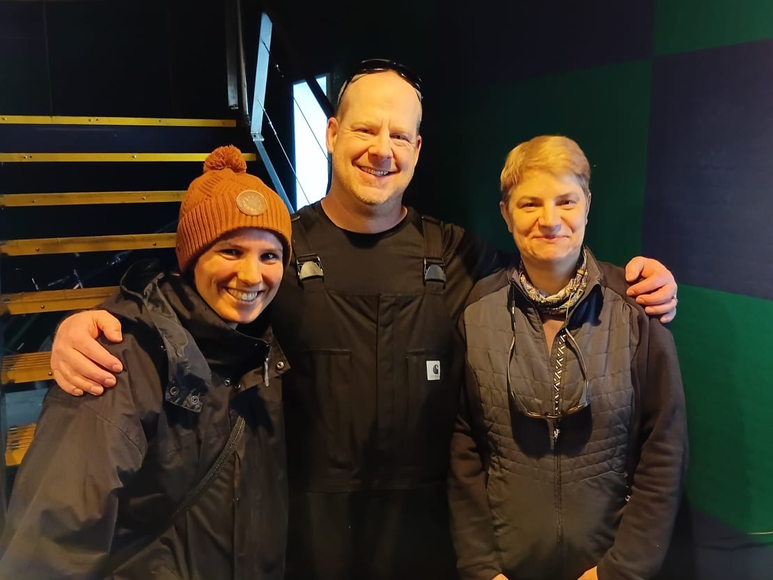 Group of three, arms around shoulders, facing camera and smiling.