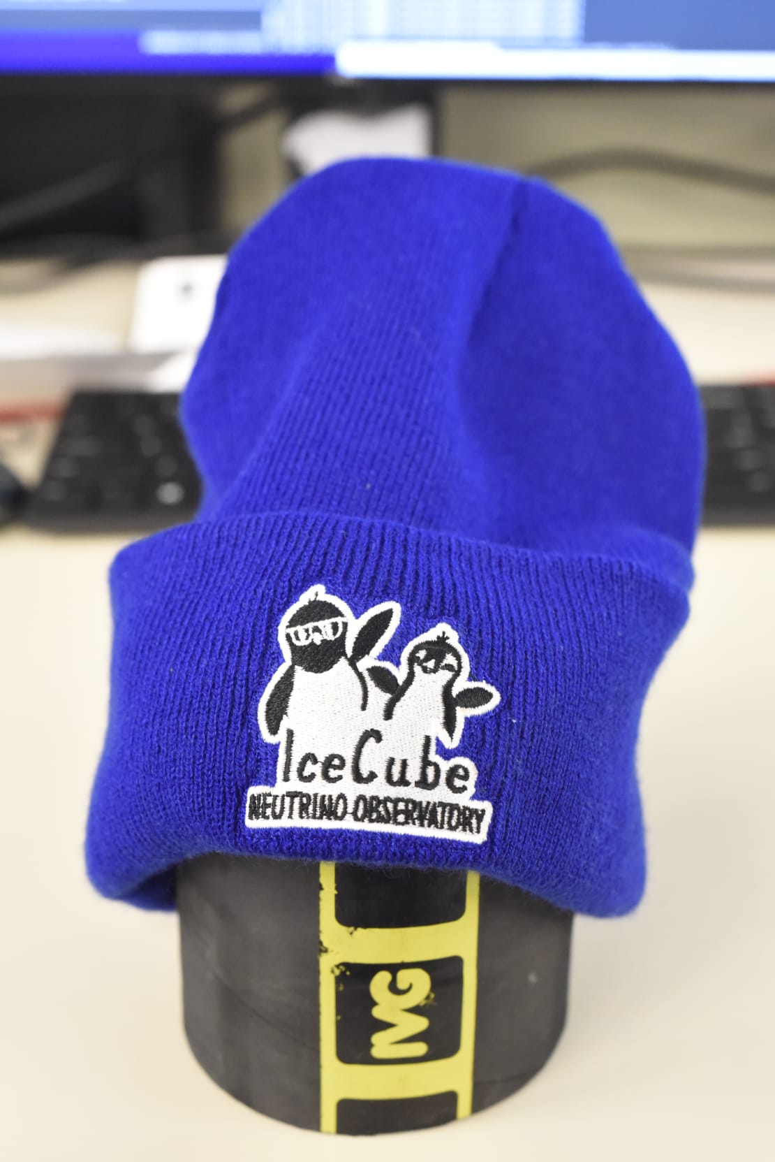 Close-up of blue knit beanie, branded with IceCube comic patch on ribbing.