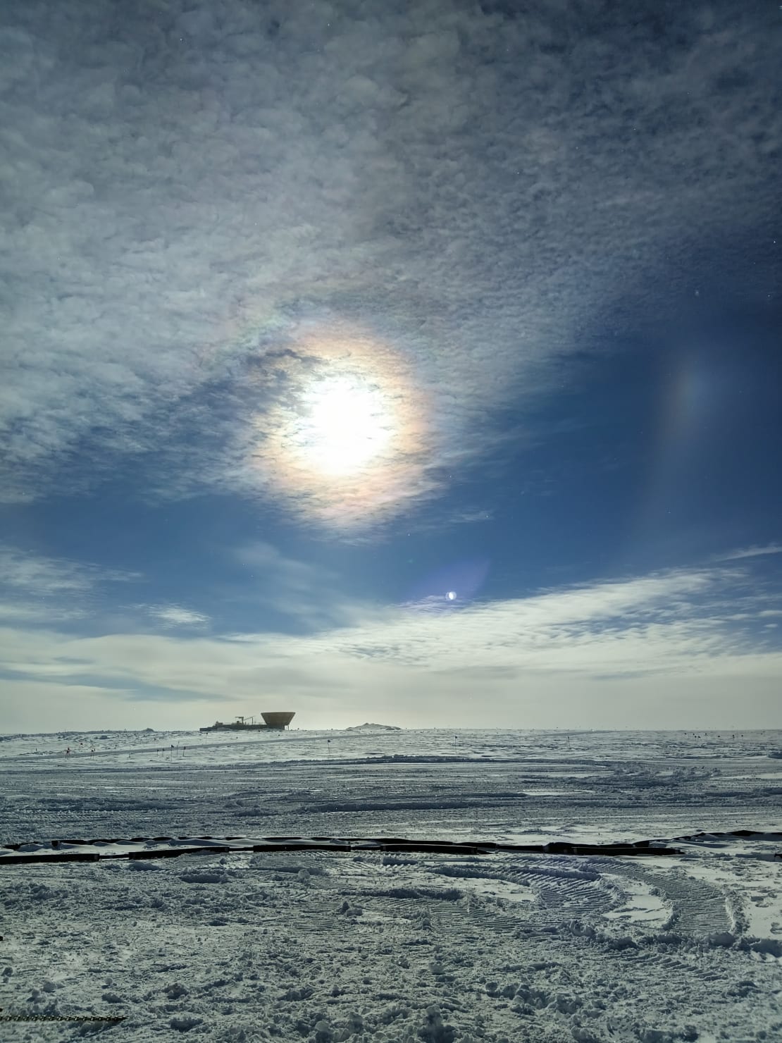 Sun with some wispy clouds in front of it, and a barely discernible halo and sun dog.