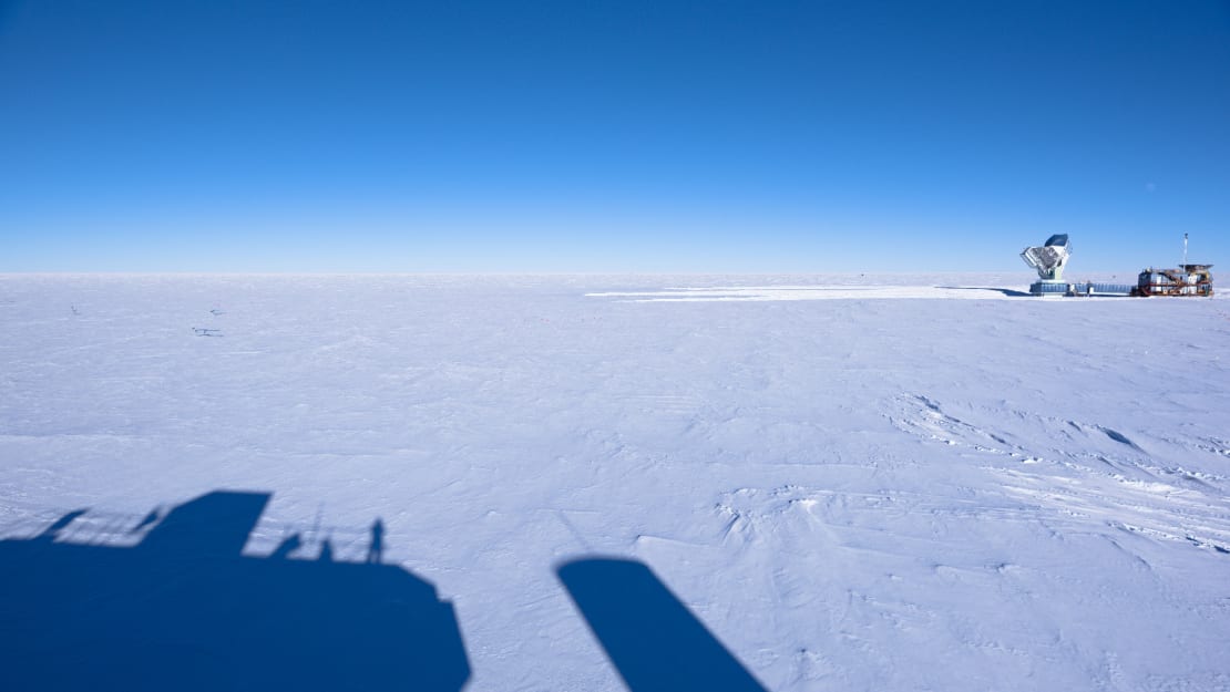 Long shadows from the IceCube Lab in the foreground, clear sky all along horizon.