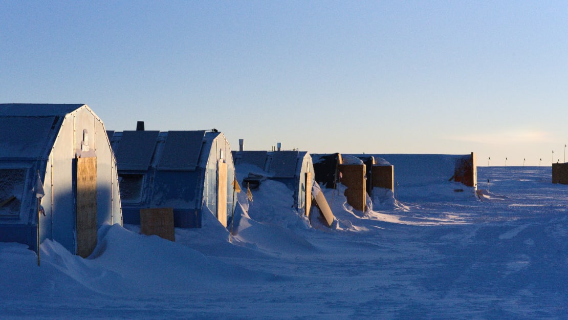 A line of hypertats (barracks) with shadows creeping up their fronts and snow drifts accumulating around them.