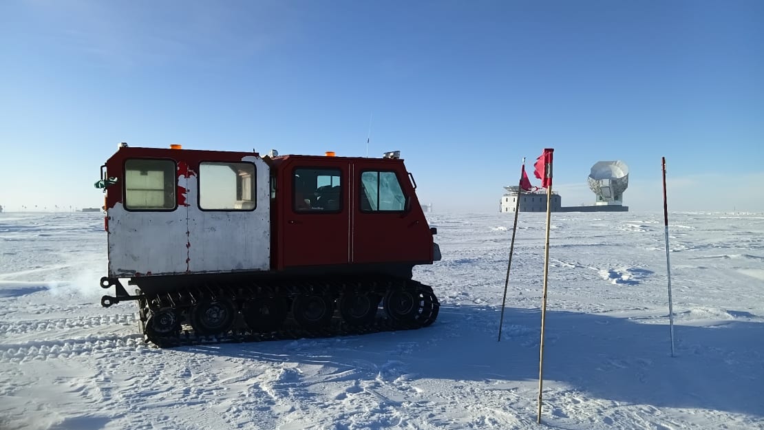 A snow vehicle parke on the ice near flag markers, South Pole telescope in distant background.
