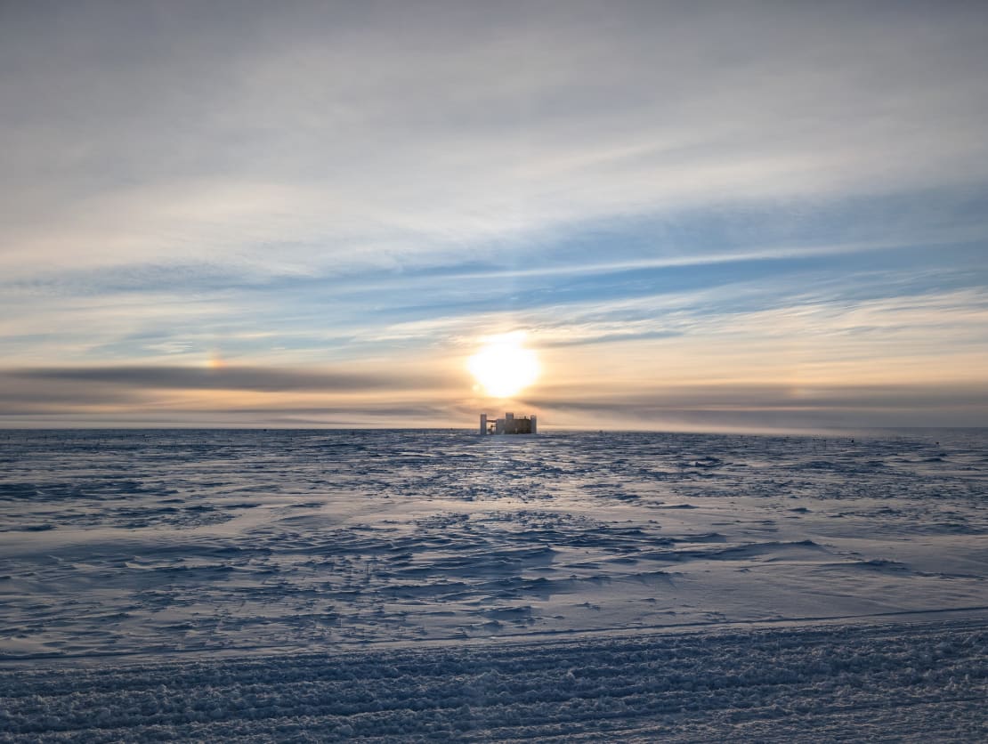 A bright sun low in a mostly cloudy sky above the IceCube Lab.