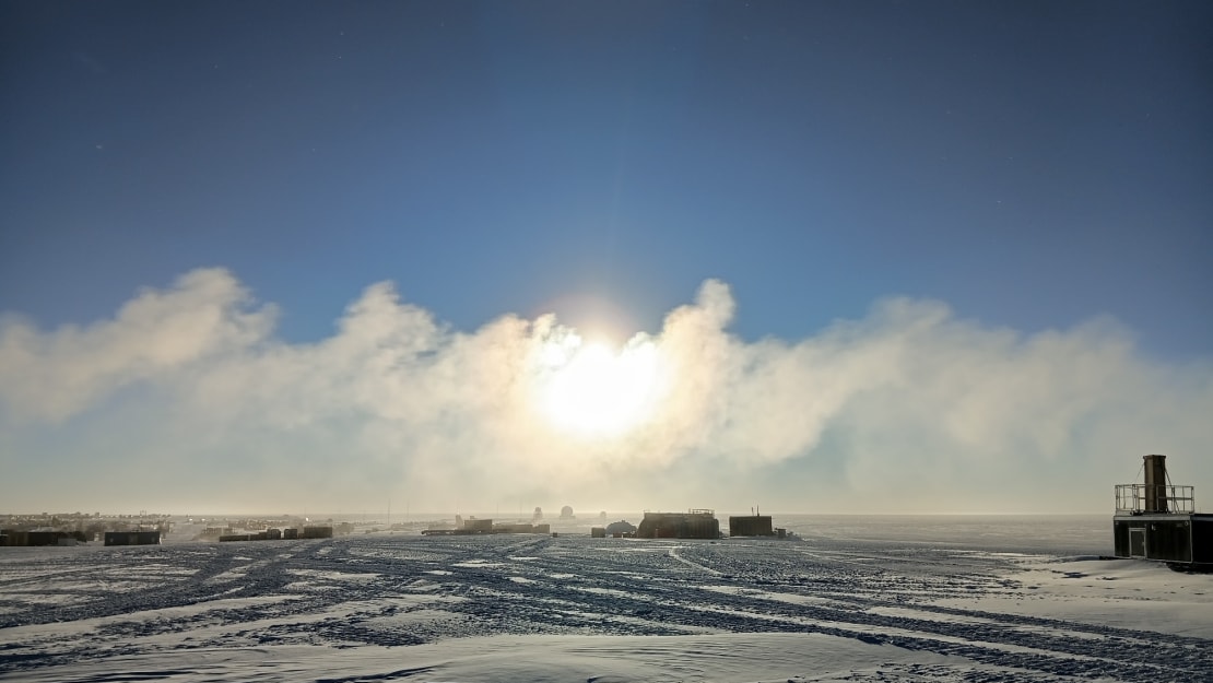Blue sky with lots of low-lying clouds covering the sun, a few structures left, right and center.