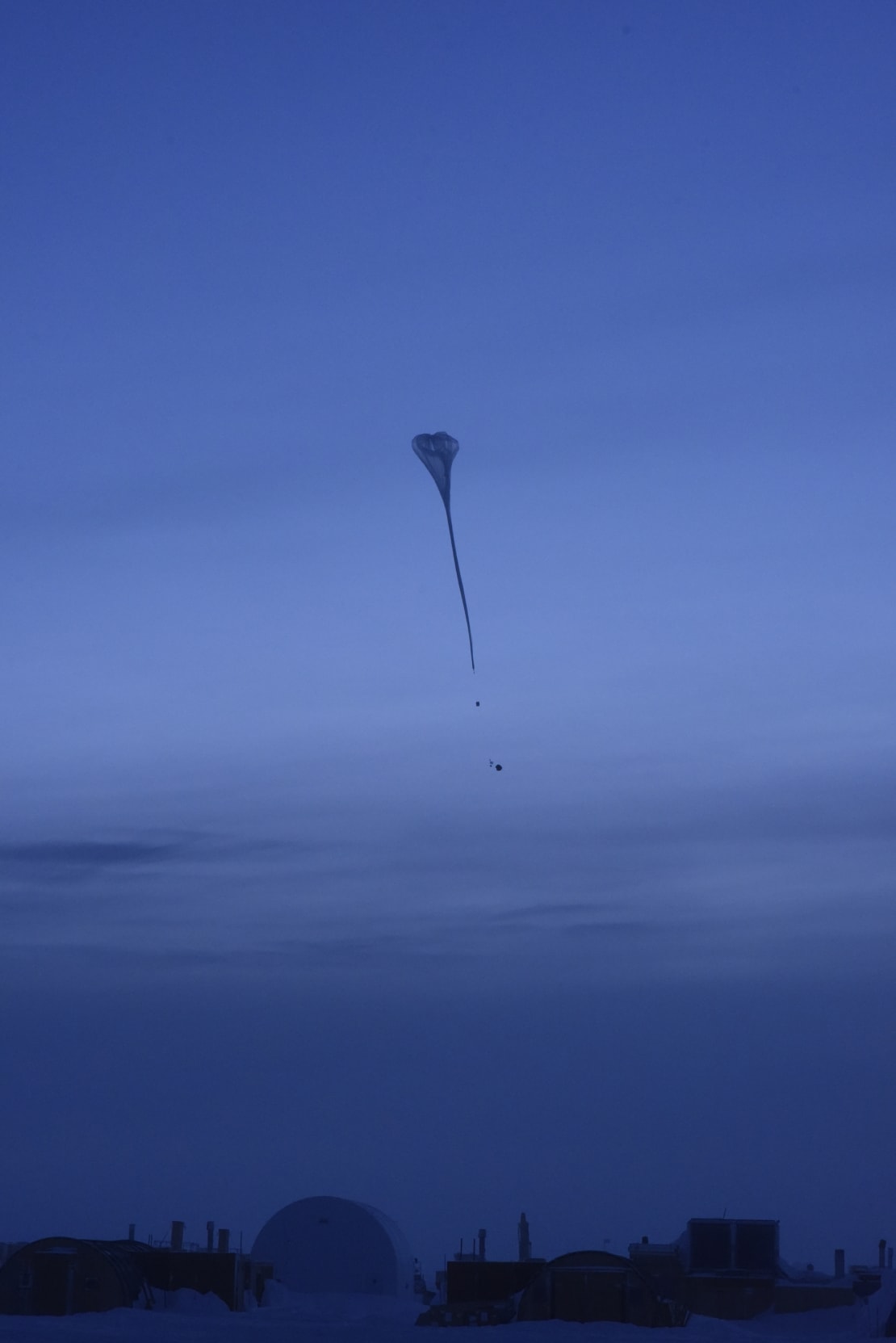 A weather balloon rising in a dark blue sky.