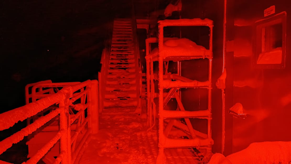 Snow-covered stairs outside South Pole station lit in red light.