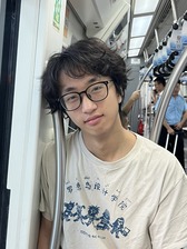 A man with black hair is leaning against a bar on a train.