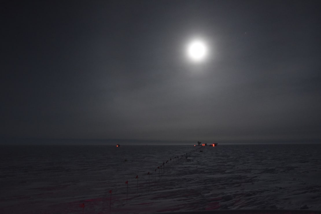 Full moon in dark sky over Dark Sector building on distant horizon.
