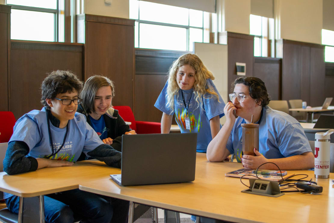 A group of students crowding around a laptop in a conference room.