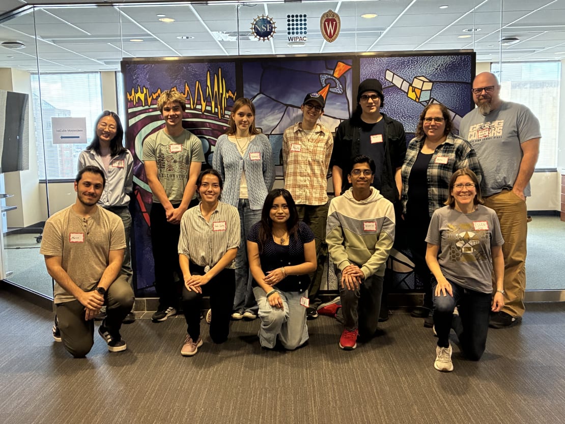 A group of people posing in front of an art mural in a lobby.