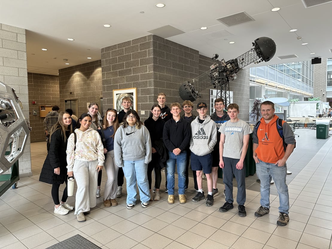 A group of students posing in front of a sculpture inside a building.