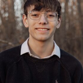 A headshot of a man with glasses and a sweater vest.