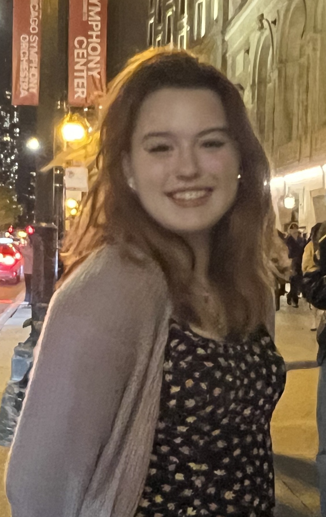A woman with long brown hair and a black top posing for a photo in a busy street.