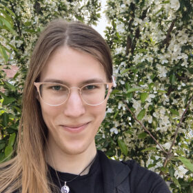 A headshot of a woman with glasses posing in front of flowers.