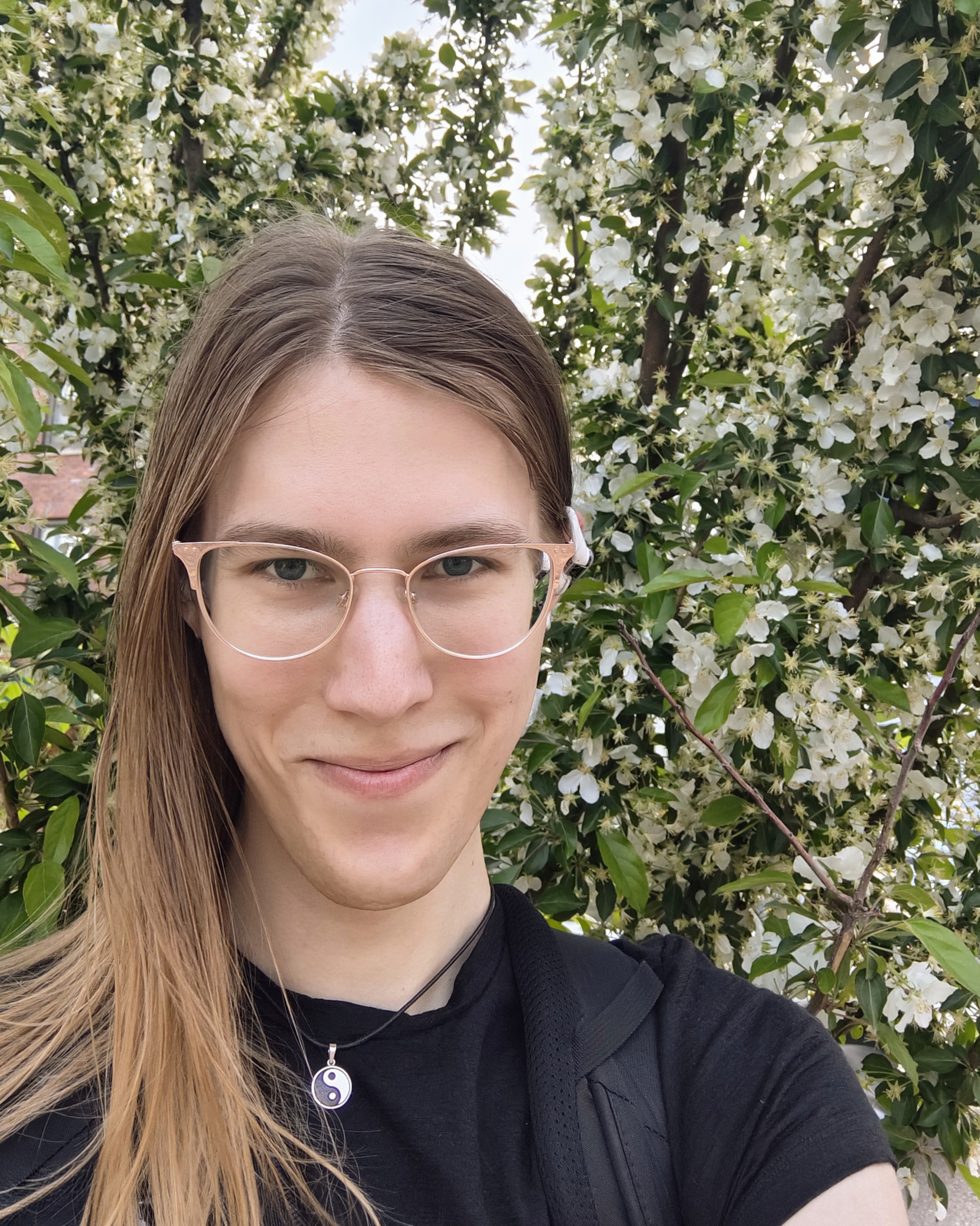 A headshot of a woman with glasses posing in front of flowers.