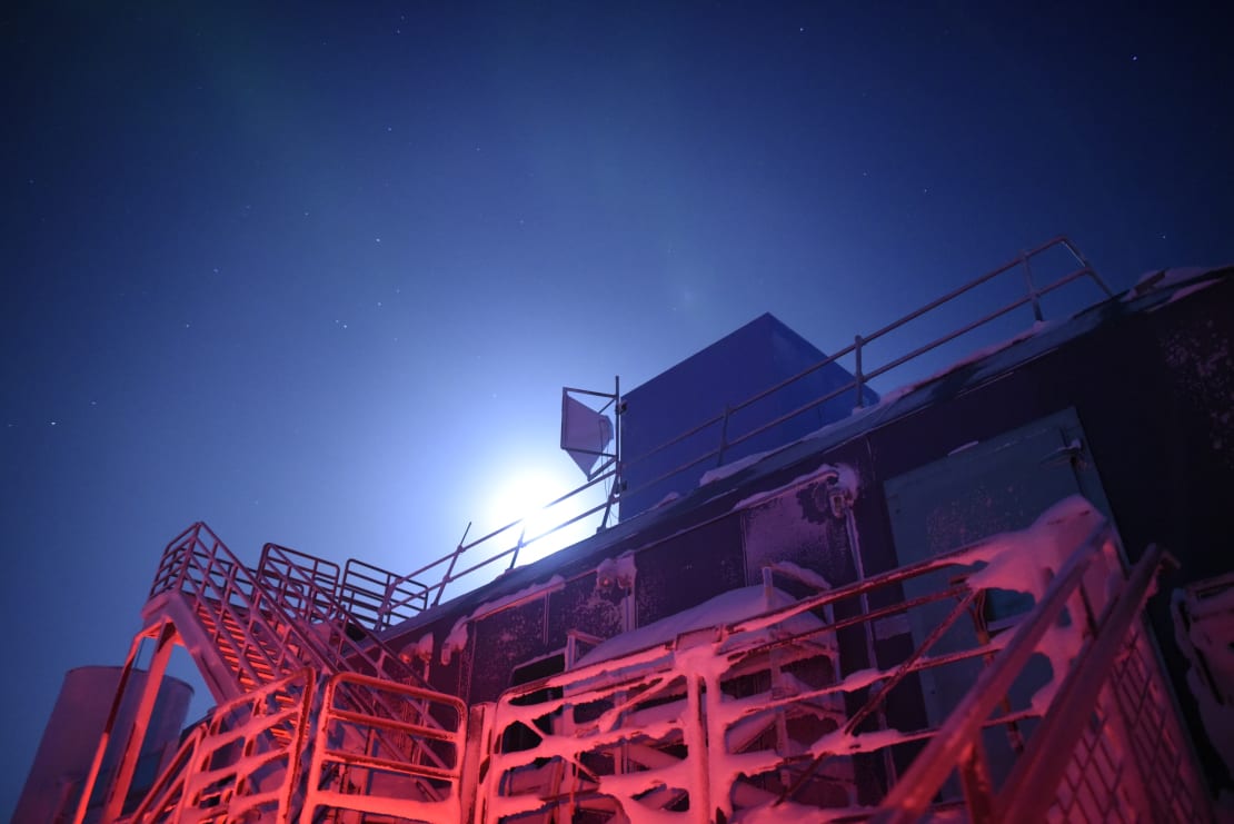 View looking up at the IceCube Lab with a bright moon peaking over the top.