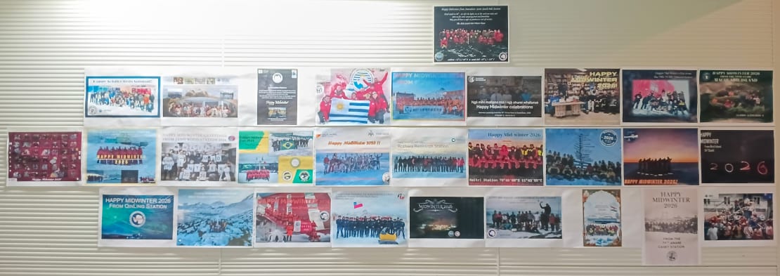 Collage of printed greetings from other Antarctic stations adorning a wall.
