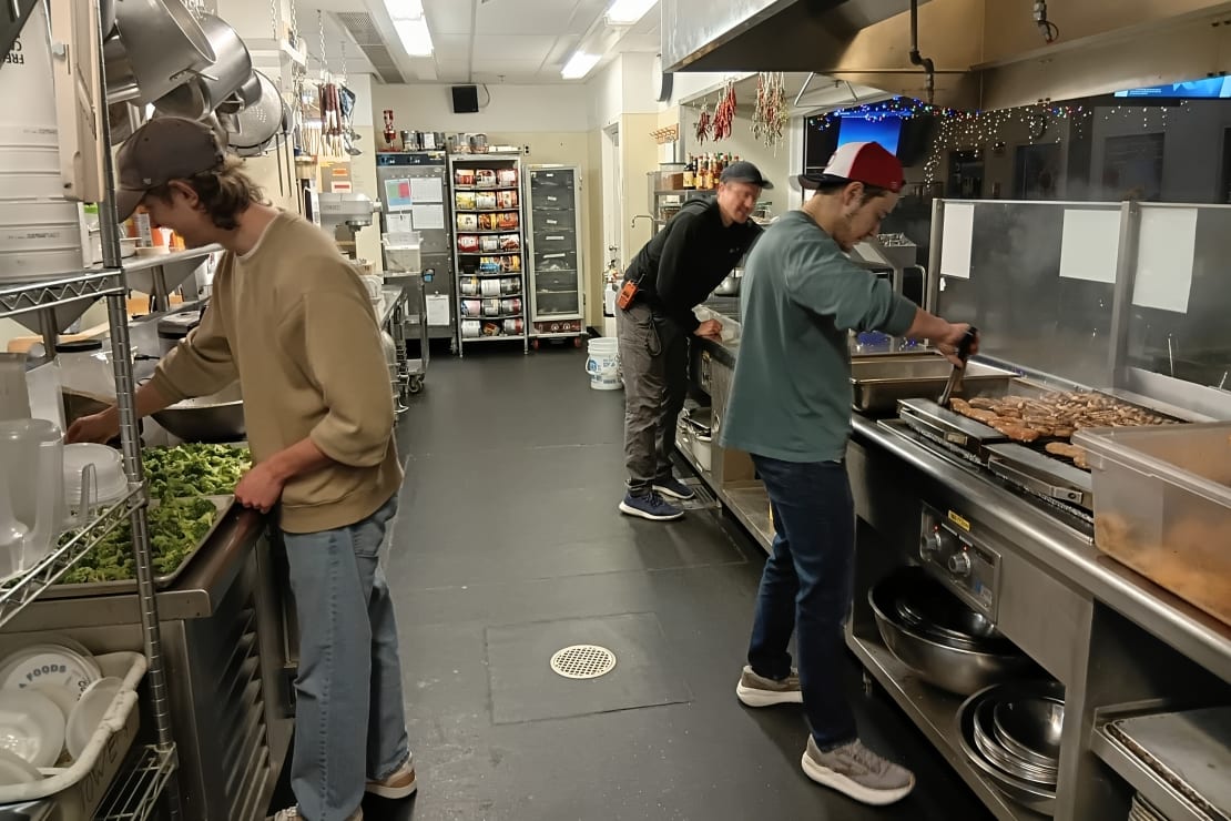 Side view of several people working at different stations of industrial kitchen.