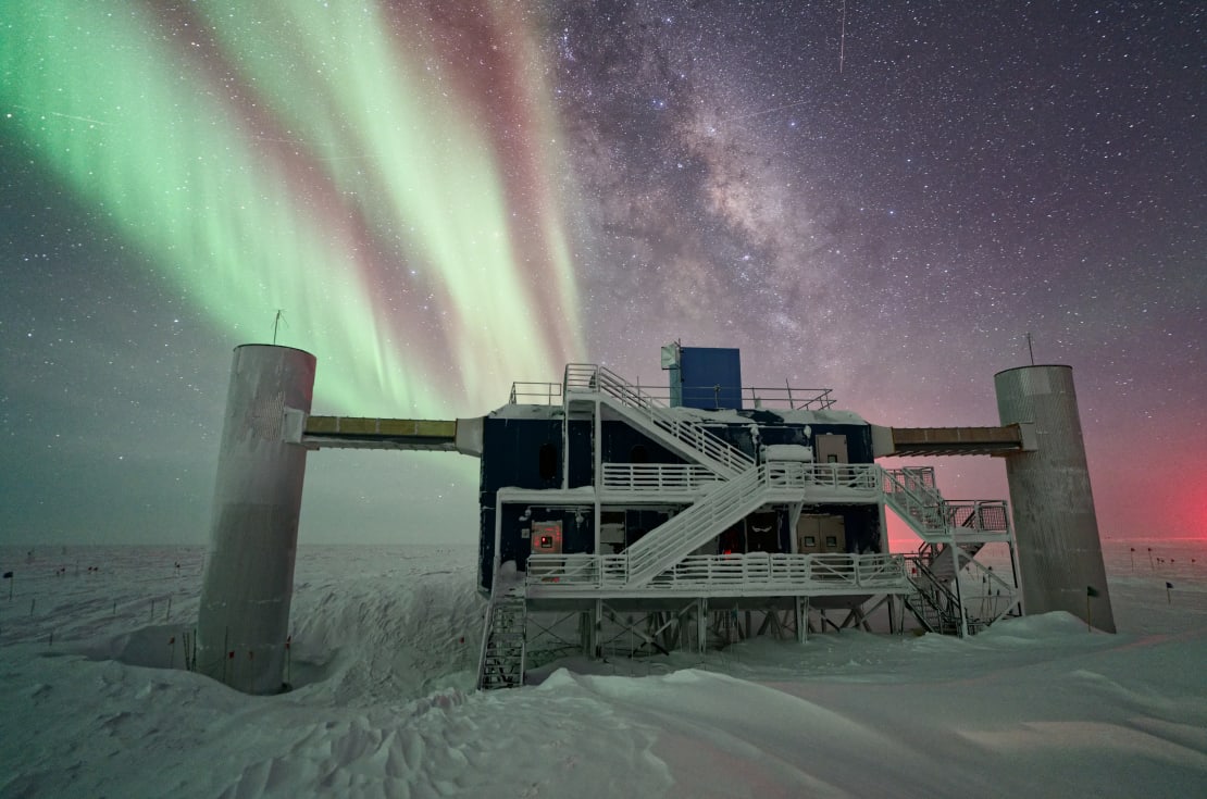 The IceCube Lab is seen with the Milky Way and auroras in the night sky at the South Pole.
