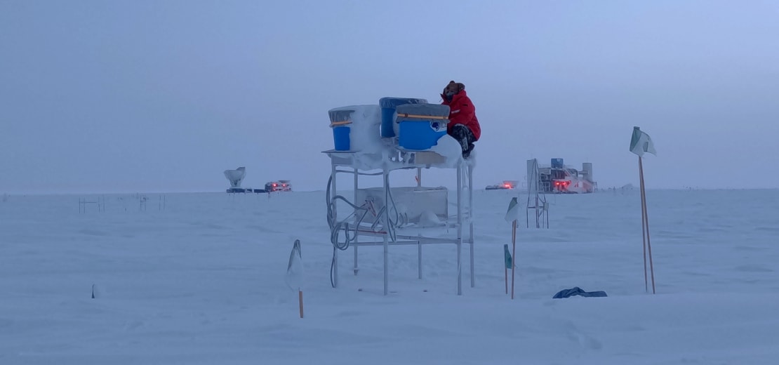Person placing covers on trio of telescopes outside on scaffolding at the South Pole.