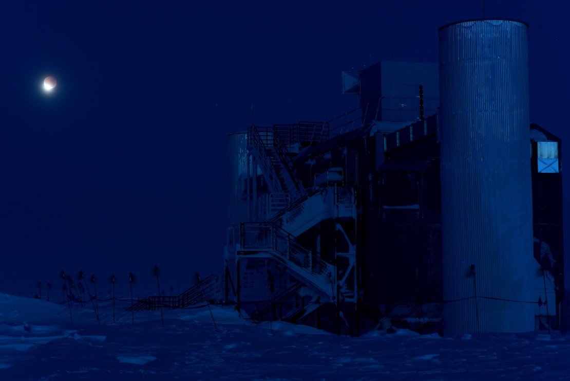 Dark image of the IceCube Lab close up, all in blues, under a partial lunar eclipse.