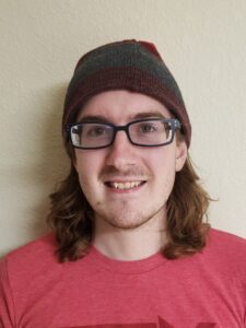 A headshot of a man wearing glasses and a beanie.