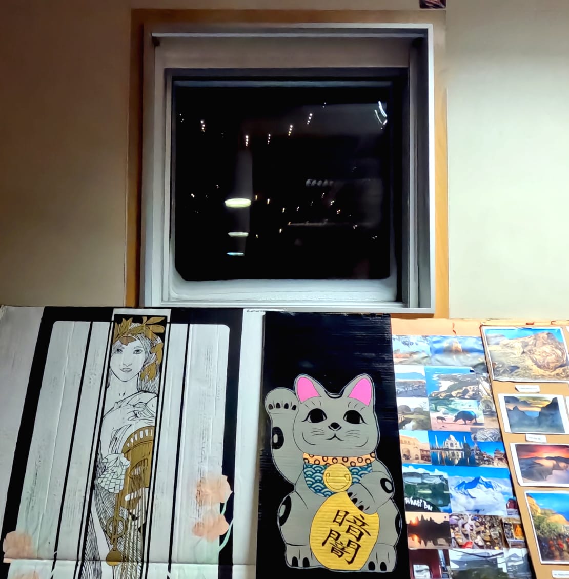 A window showing darkness outside and reflections from the lights inside, with artistic panels leaning against wall below it.