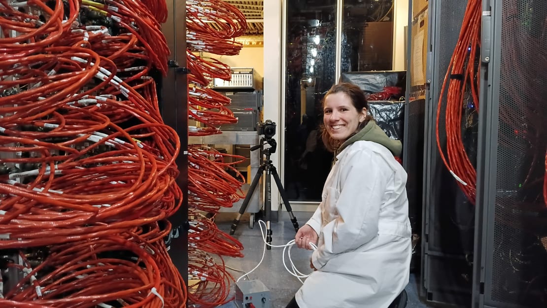Side view of person kneeling in front of computer racks with mass of orange cables.